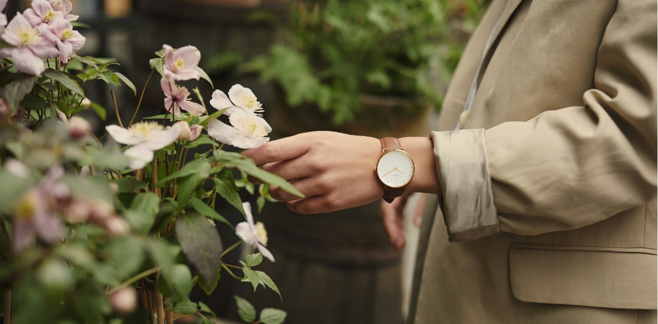 a hand wearing a watch and touching a flower
