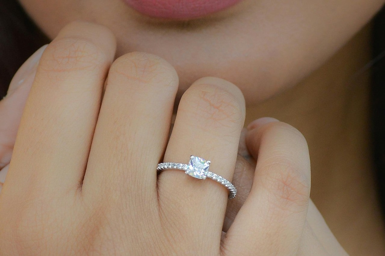 A close-up of a woman’s hand resting under her chin, adorned with an elegant engagement ring.