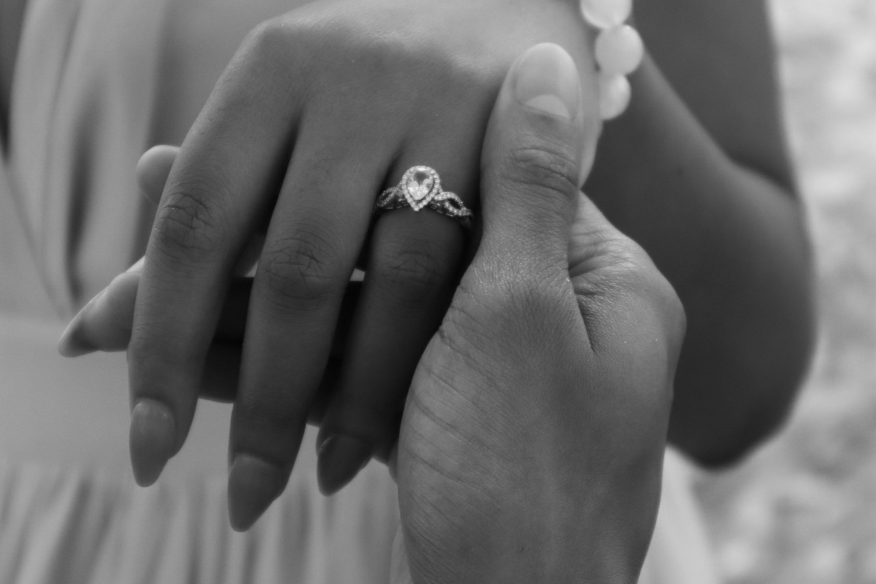 black and white photo of a man holding a woman’s hand, adorned with a pear shape ring