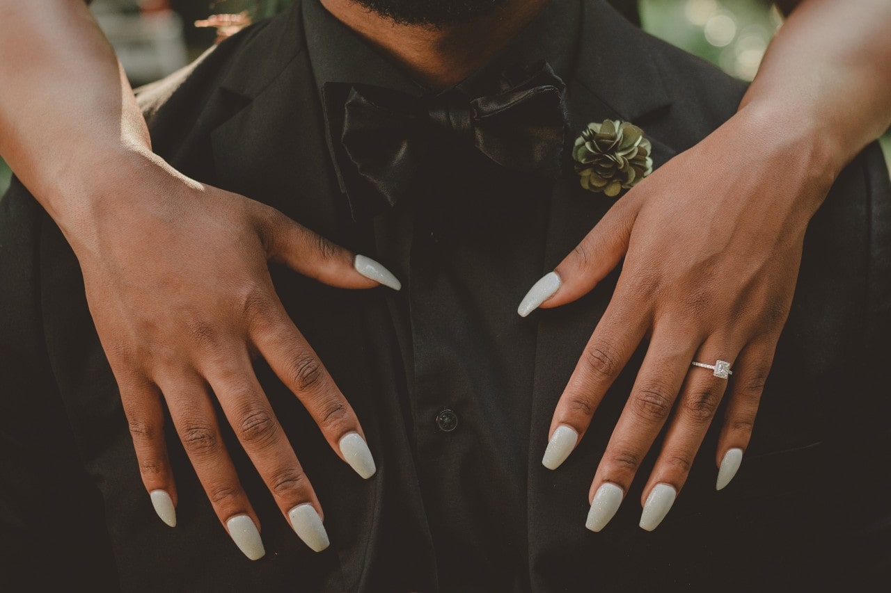 a woman drapes her hands in front of a man’s chest, wearing a princess cut ring.