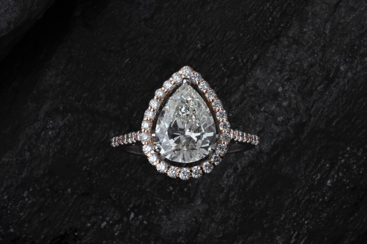 a pear shape halo setting engagement ring against a textured black background