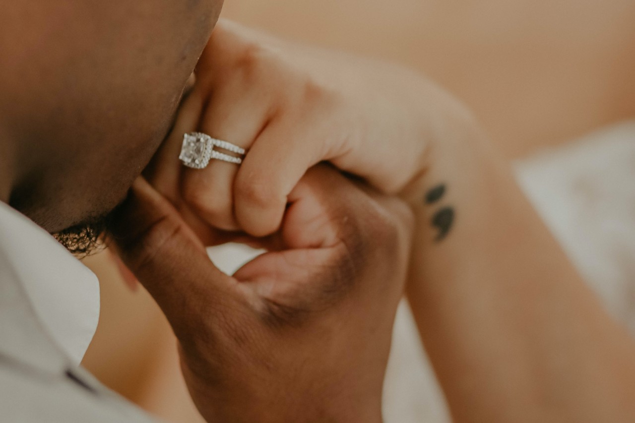 A man kissing a woman’s hand, adorned with a princess cut engagement ring.