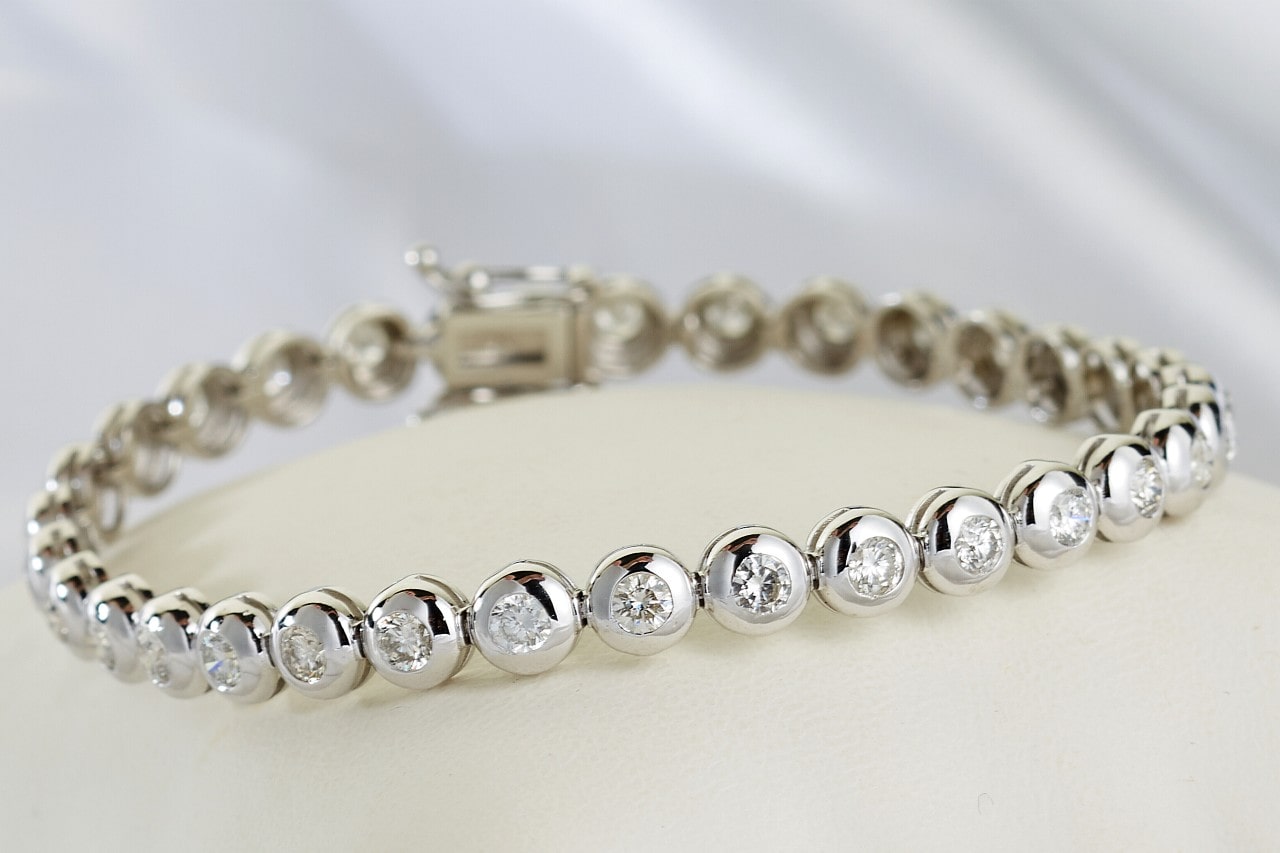 A white gold tennis bracelet featuring bezel set, round cut diamonds.