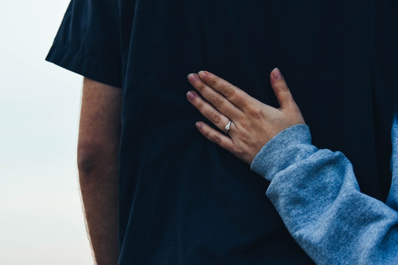 a casual couple pose, the woman wearing a halo engagement ring.