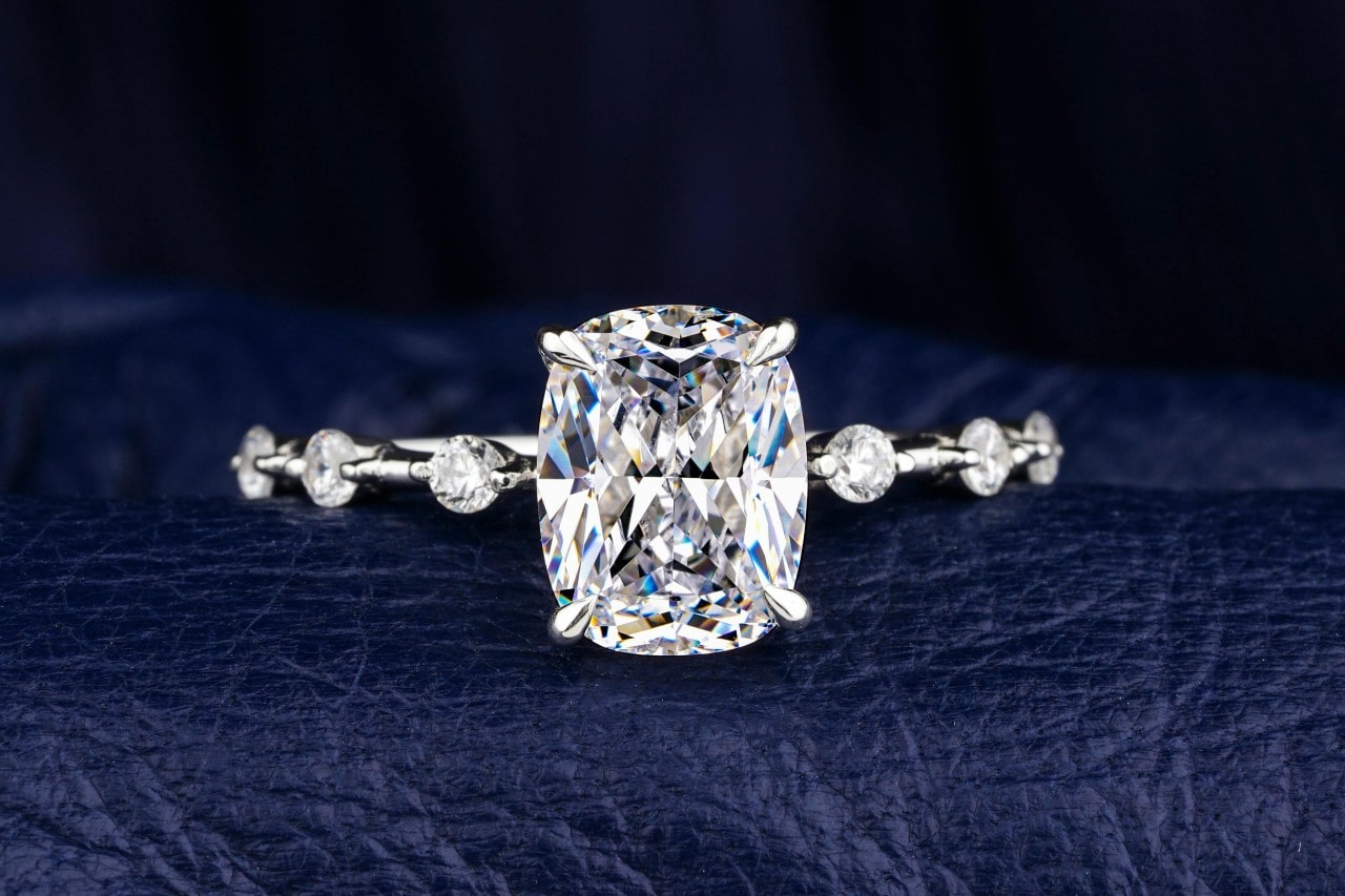 An elegant and distinctive diamond engagement ring displayed on a blue leather backdrop.