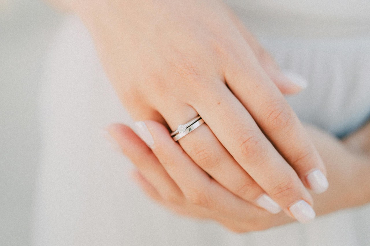 A close-up of a woman’s hands, one adorned with a round cut engagement ring and wedding band.