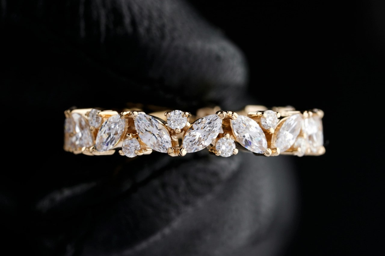 A close-up image of a yellow gold wedding band featuring marquise and round cut diamonds.