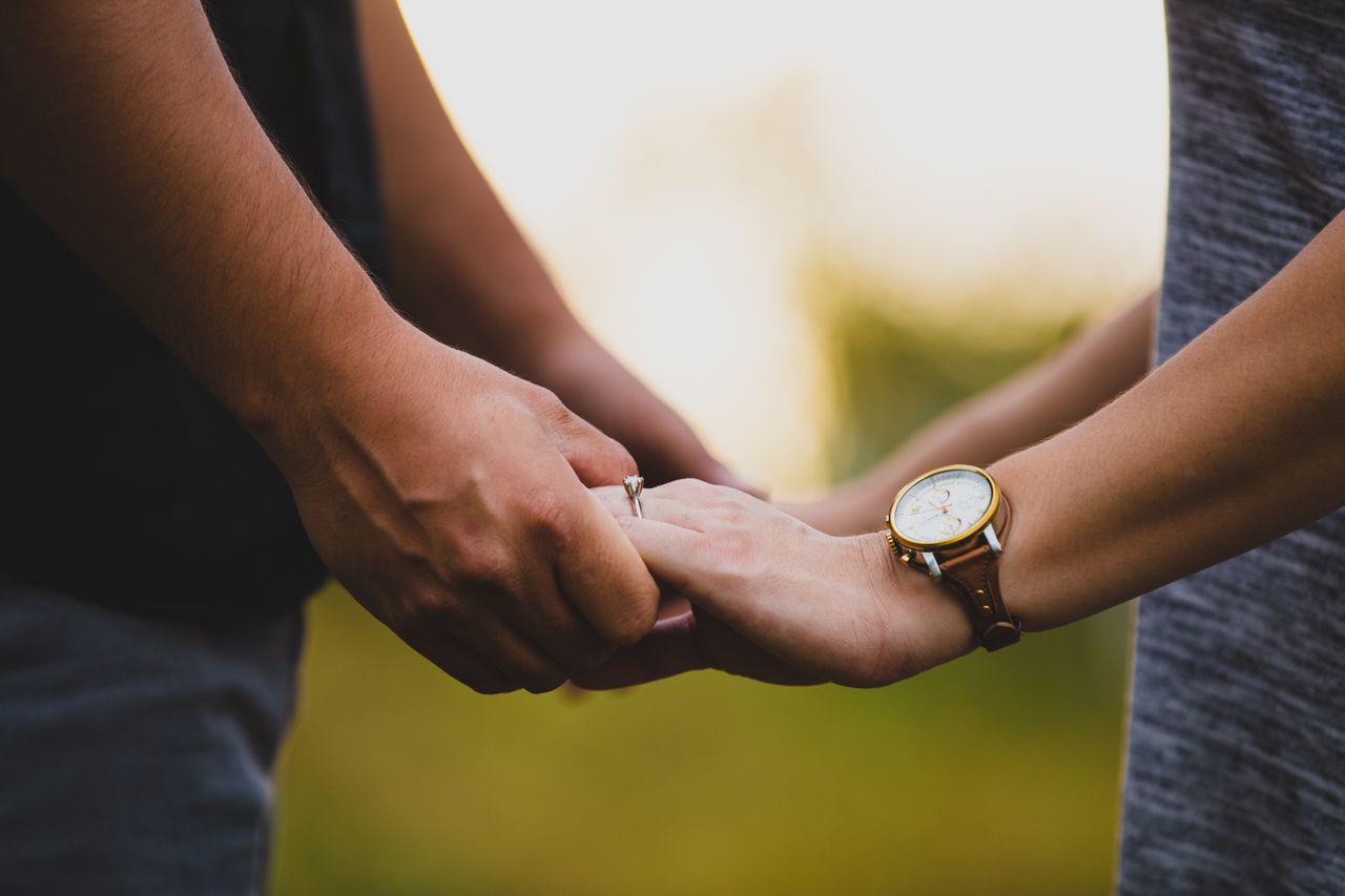 a couple holding hands, the woman wearing a solitaire engagement ring.