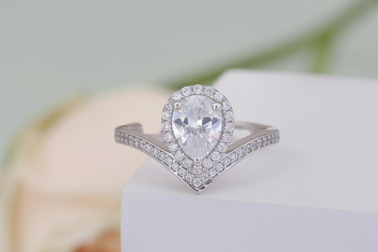 close up image of a halo set, pear shape engagement ring on a white box