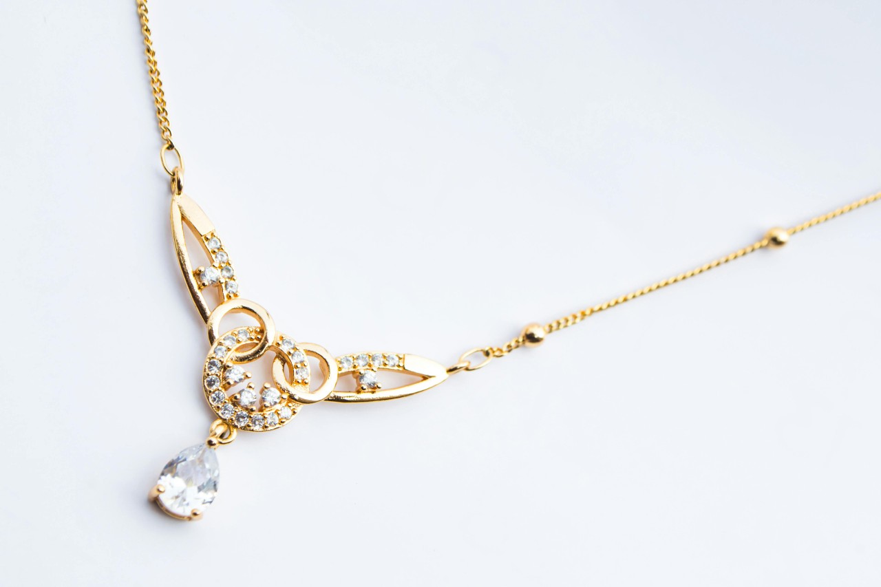 A yellow gold diamond necklace featuring a pear shape center stone and round cut accents.