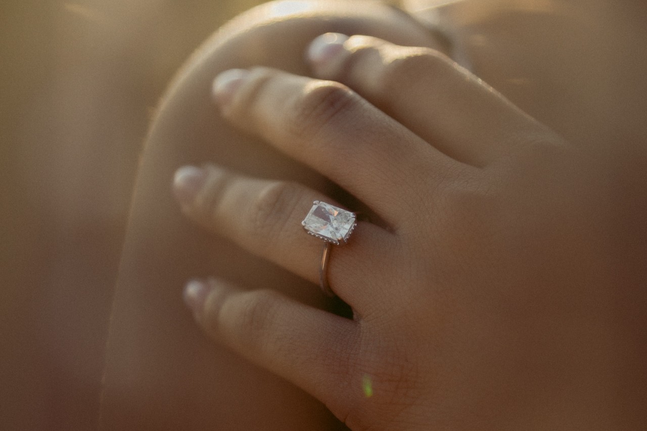 A woman’s hand, adorned with an emerald cut engagement ring, resting on her shoulder.