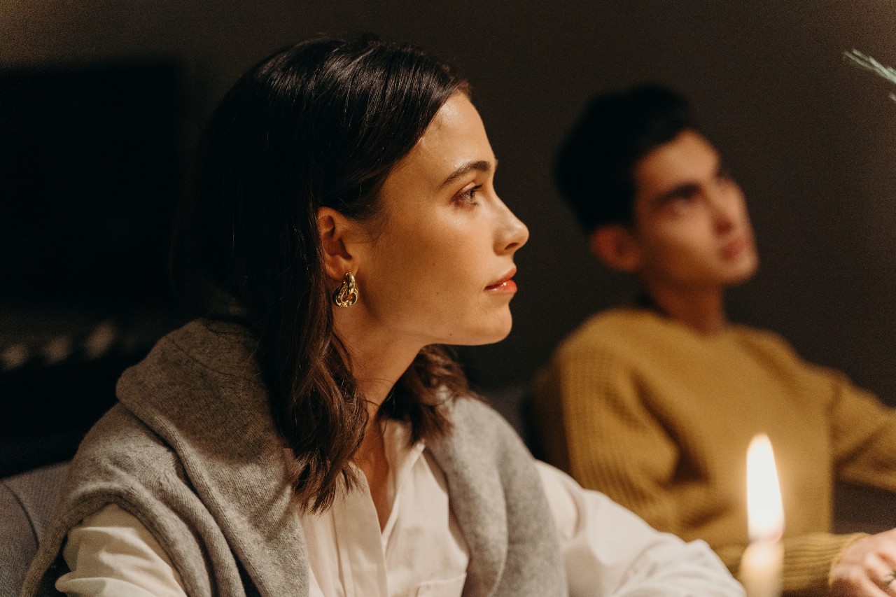 a lady wearing a gold earring sitting by a candle