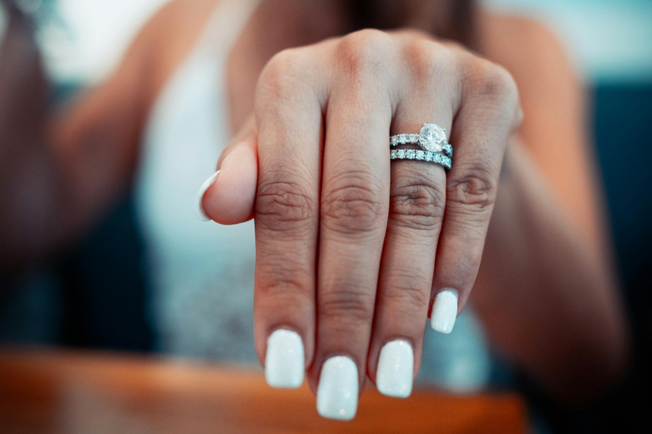 a woman’s extended hand showing off a round cut engagement ring and wedding band