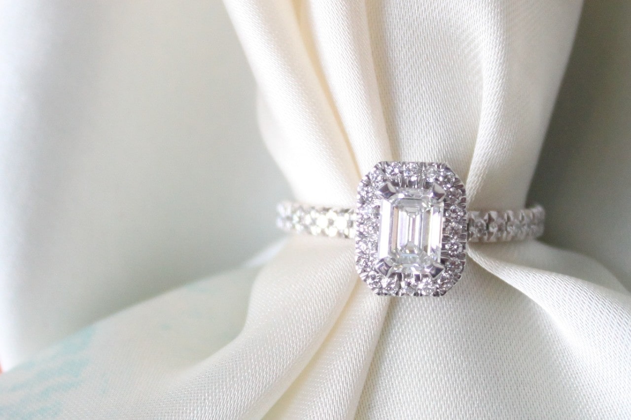 an emerald cut halo engagement ring with a white cloth threaded through it