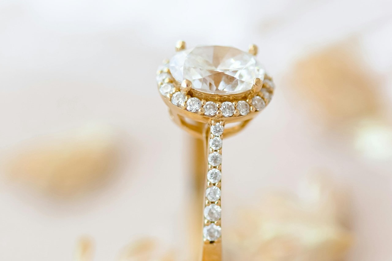 close up image of a yellow gold oval cut halo engagement ring with side stones