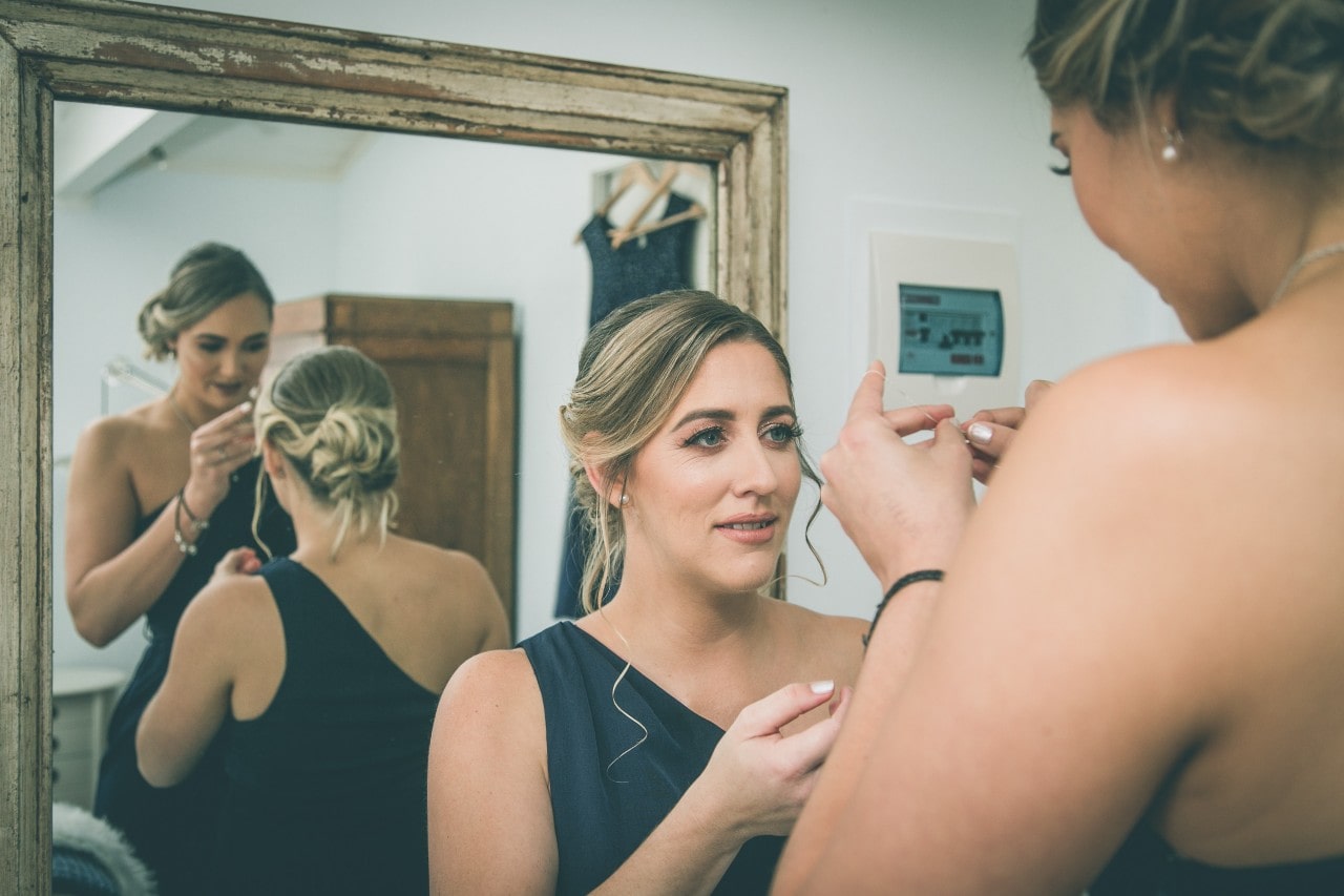 Two bridesmaids helping each other put on jewelry