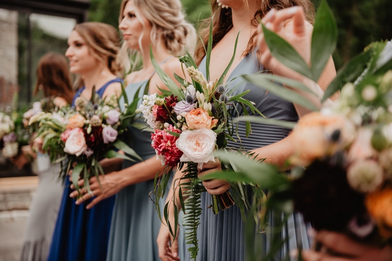 Two bridesmaids and the maid of honor holding elegant bouquets as they stand at the altar.