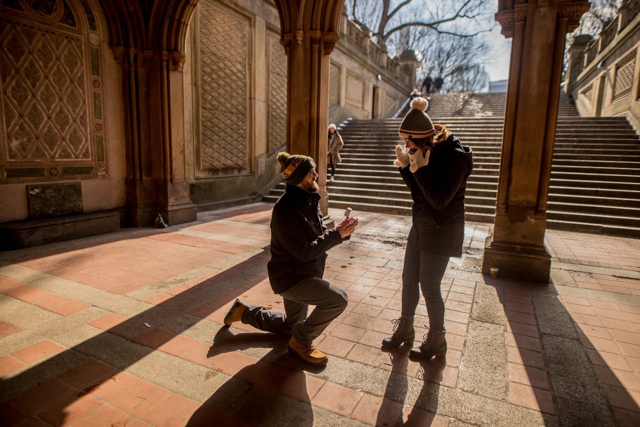 A man proposing to his partner under a stone archway.