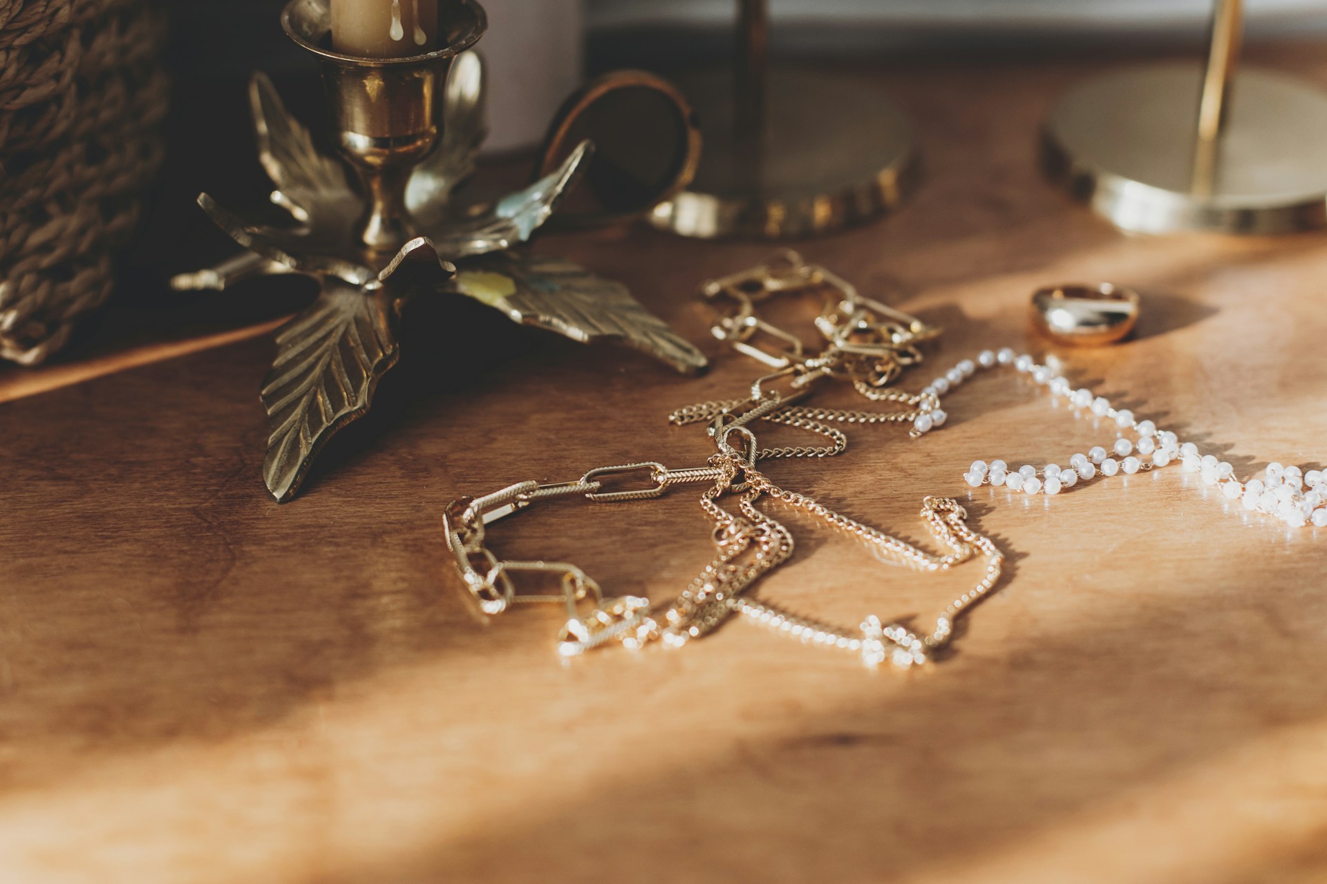 An overhead photo of a small selection of delicate necklaces and a gold band displayed on a wooden tabletop.